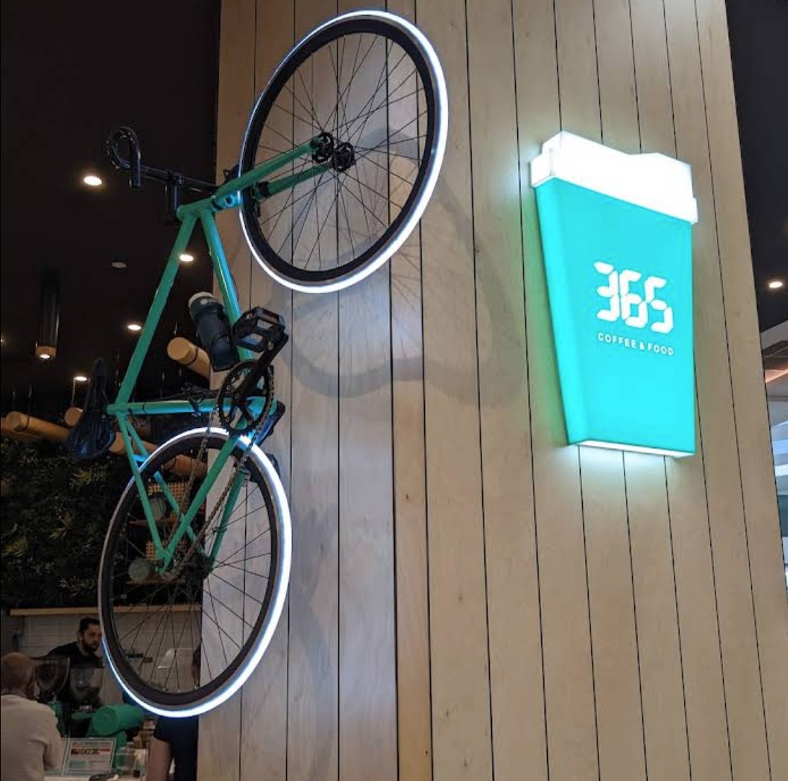 Illuminated bicycle landmark mounted on the wall beside the 365 Coffee logo sign