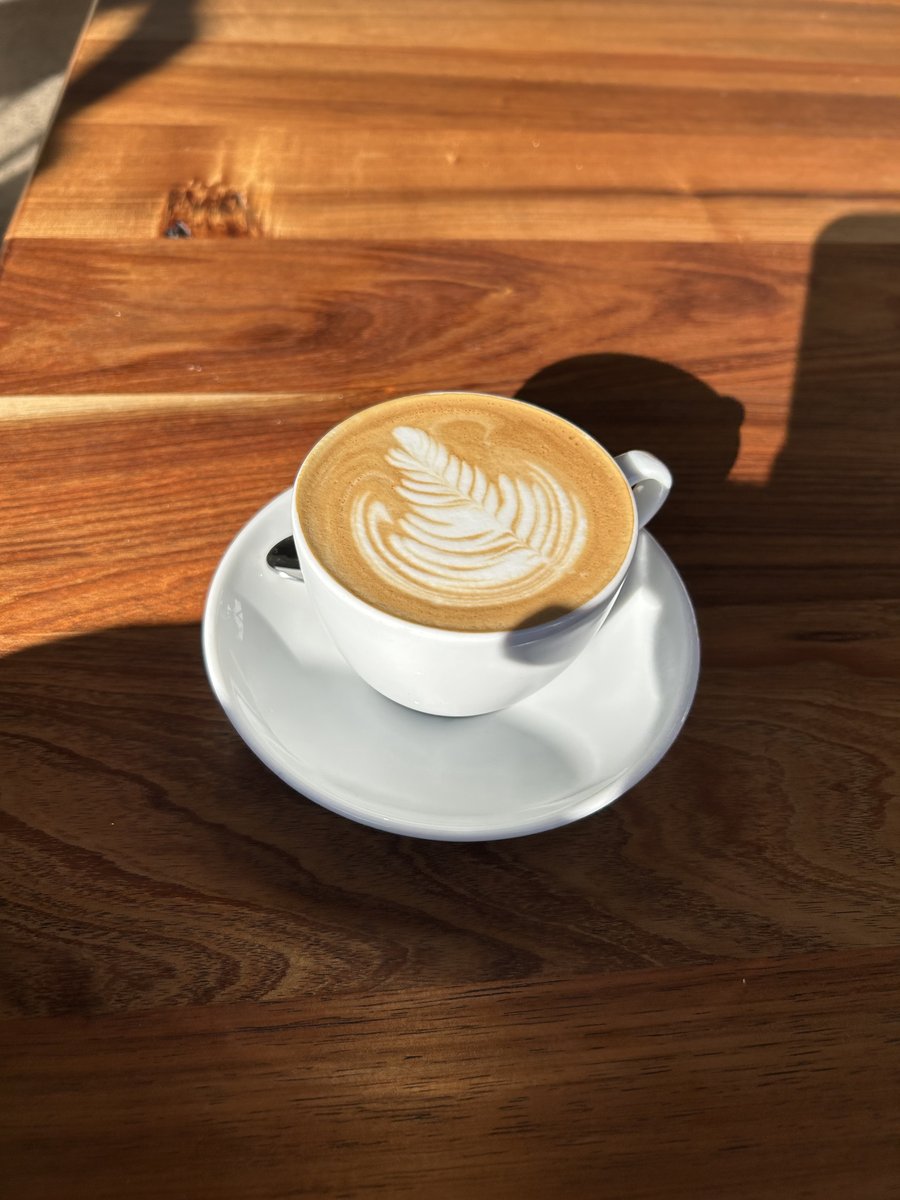 Latte with leaf art on a sunlit wooden table at Baker of Things
