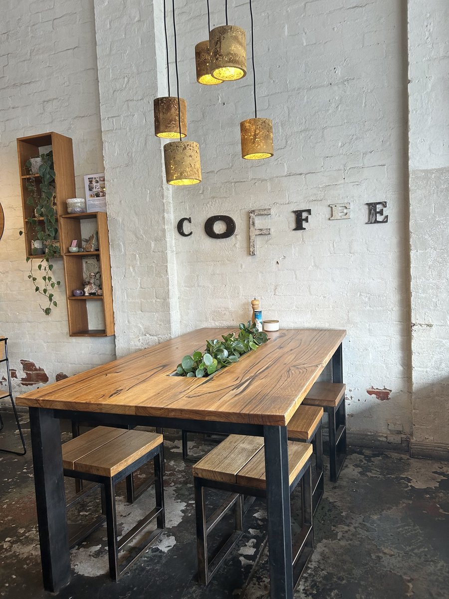 Communal wooden table beneath pendant lights with COFFEE lettering on the brick wall