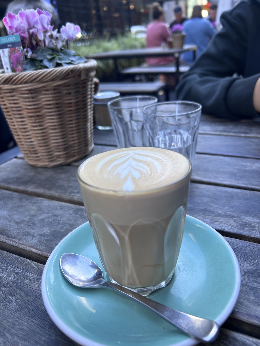 Latte with leaf-pattern art on an outdoor table at Two Birds One Stone